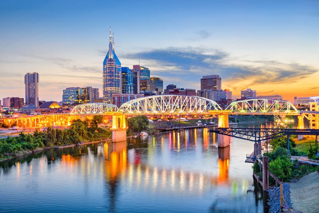 Skyline von Nashville, Tennessee, bei Sonnenuntergang mit beleuchteter Brücke über den Cumberland River und modernen Hochhäusern im Hintergrund.