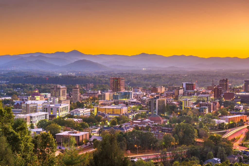 Panoramablick auf die Skyline von Asheville, North Carolina, mit den Bergen der Blue Ridge Mountains bei Sonnenuntergang.